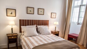 Ein ordentlich bezogenes Bett mit Streifenmuster, zwei Nachttische mit Lampen und gerahmte Bilder an der Wand.