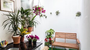 Ein kleiner Patio-Bereich mit einer Holzbank, Topfpflanzen und einem gerahmten Bild an der Wand.