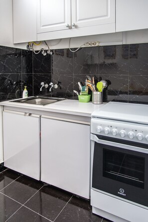 A modern kitchen with white cabinets, a black tiled backsplash, a stainless steel sink, and a white stove.