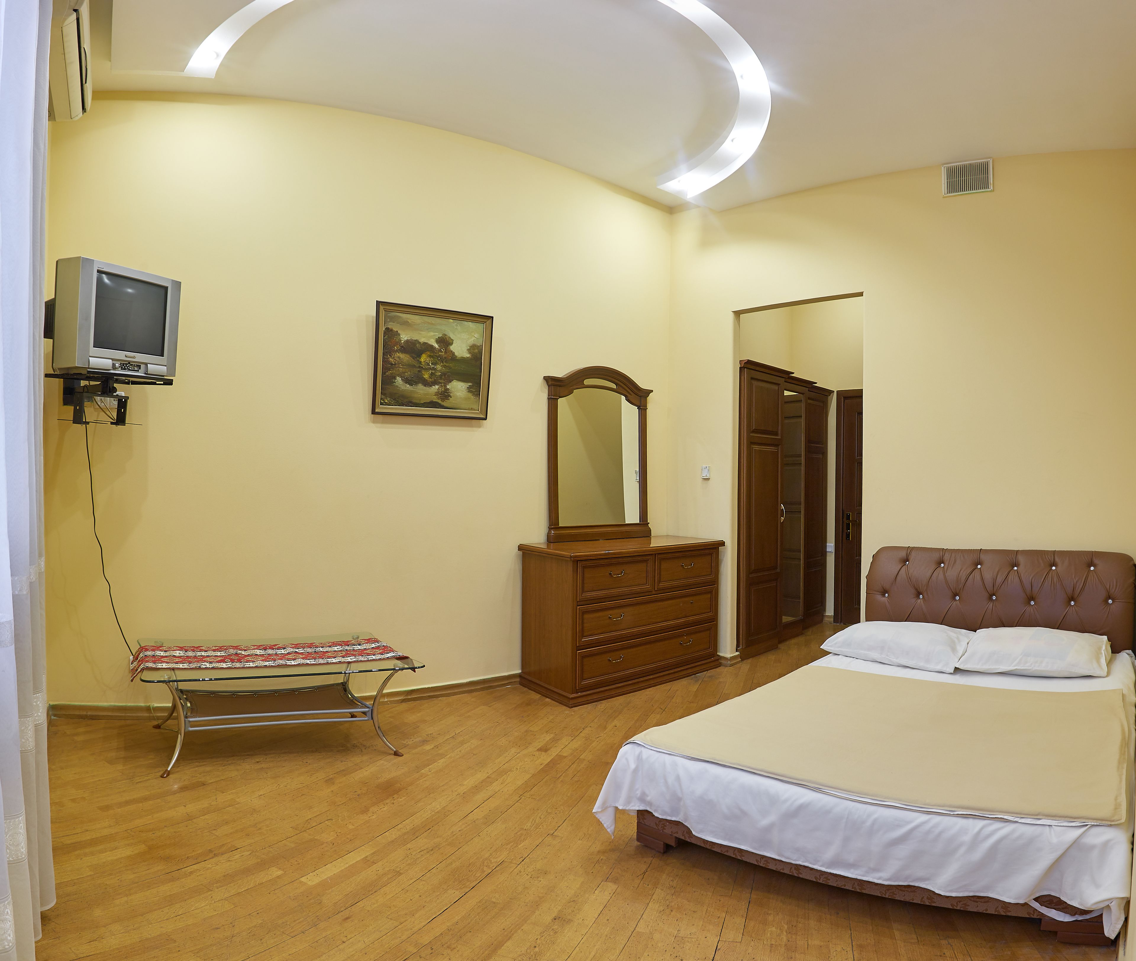 A bedroom with a bed, dresser, mirror, and a television.