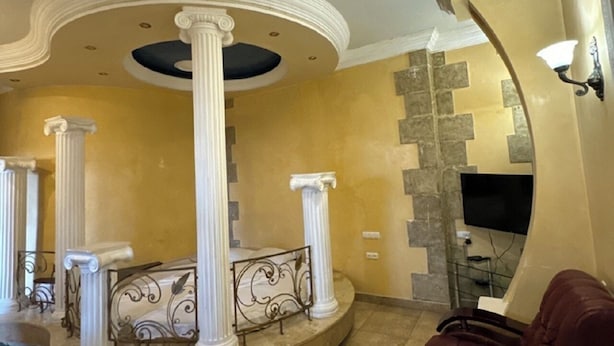 A living room with a circular seating area, columns, a TV, and a fireplace. - Bella Hotel (Yerevan)