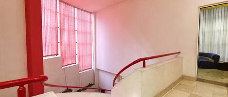 A staircase with red railings and a handrail, leading to a landing with a view of a room with a blue sofa and a window with vertical blinds.