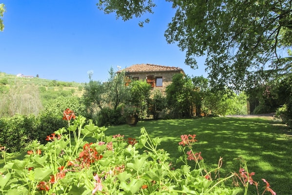 A stone house with a tiled roof, surrounded by lush greenery and a well-maintained lawn.