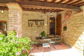 A stone-walled patio with a table and chairs, a hanging light fixture, and a wooden door.