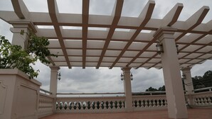 A covered outdoor area with a pergola structure, tiled flooring, and decorative railings.