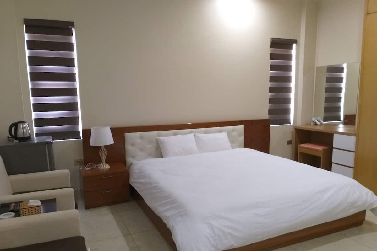 A hotel room with a large bed, bedside tables, a chair, a desk, and a mirror.