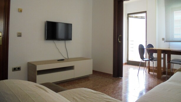 Ein Hotelzimmer mit einem Bett, einem an der Wand befestigten Fernseher, einem Schreibtisch mit Stuhl und einer Tür, die auf einen Balkon führt.