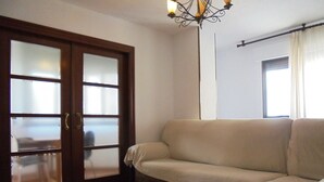 Ein Wohnzimmer mit einem beigefarbenen Sofa, einer Holztür mit satinierten Glasscheiben und einer Kristallleuchtre.
