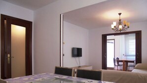 Ein Hotelzimmer mit Esstisch, Stühlen, Fernseher, einer Kristallleuchtre und einem Bett.