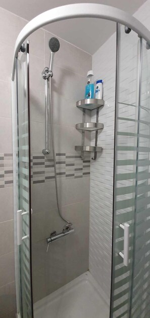 Eine Duschkabine mit Glaswänden, einer Handbrause, einer Glastür und Ablage für Toilettenartikel.