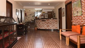 Rebuda d'hotel amb una escala de fusta, un taulell de recepció i una zona de seients amb coixins taronja.