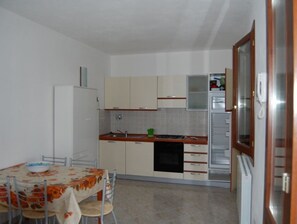 Compact kitchen with a refrigerator, sink, and dishwasher, and a dining area with a table and chairs.