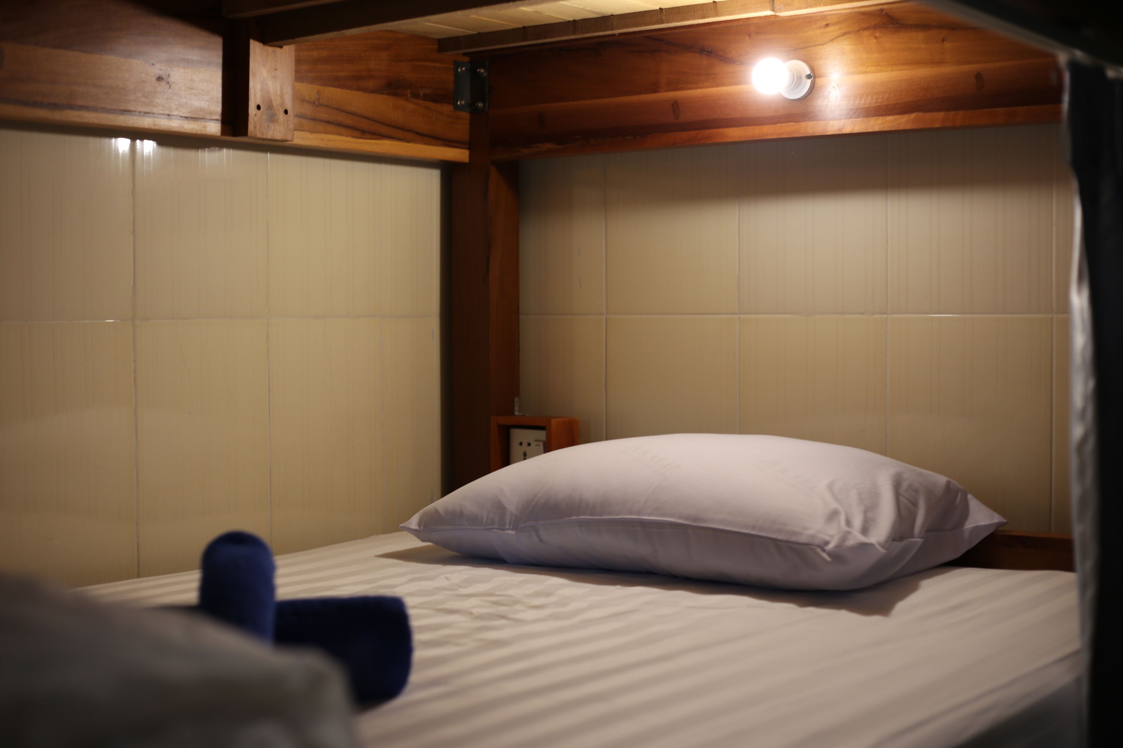 A single bed with a white pillow in a room with wooden ceiling beams and white walls.