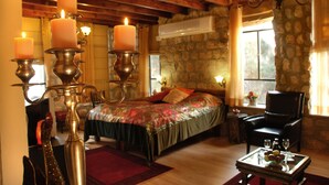 A cozy room with a bed, a chair, a table with fruit, and candles on stands. - Beit Shalom Historical Boutique Hotel (Metula)