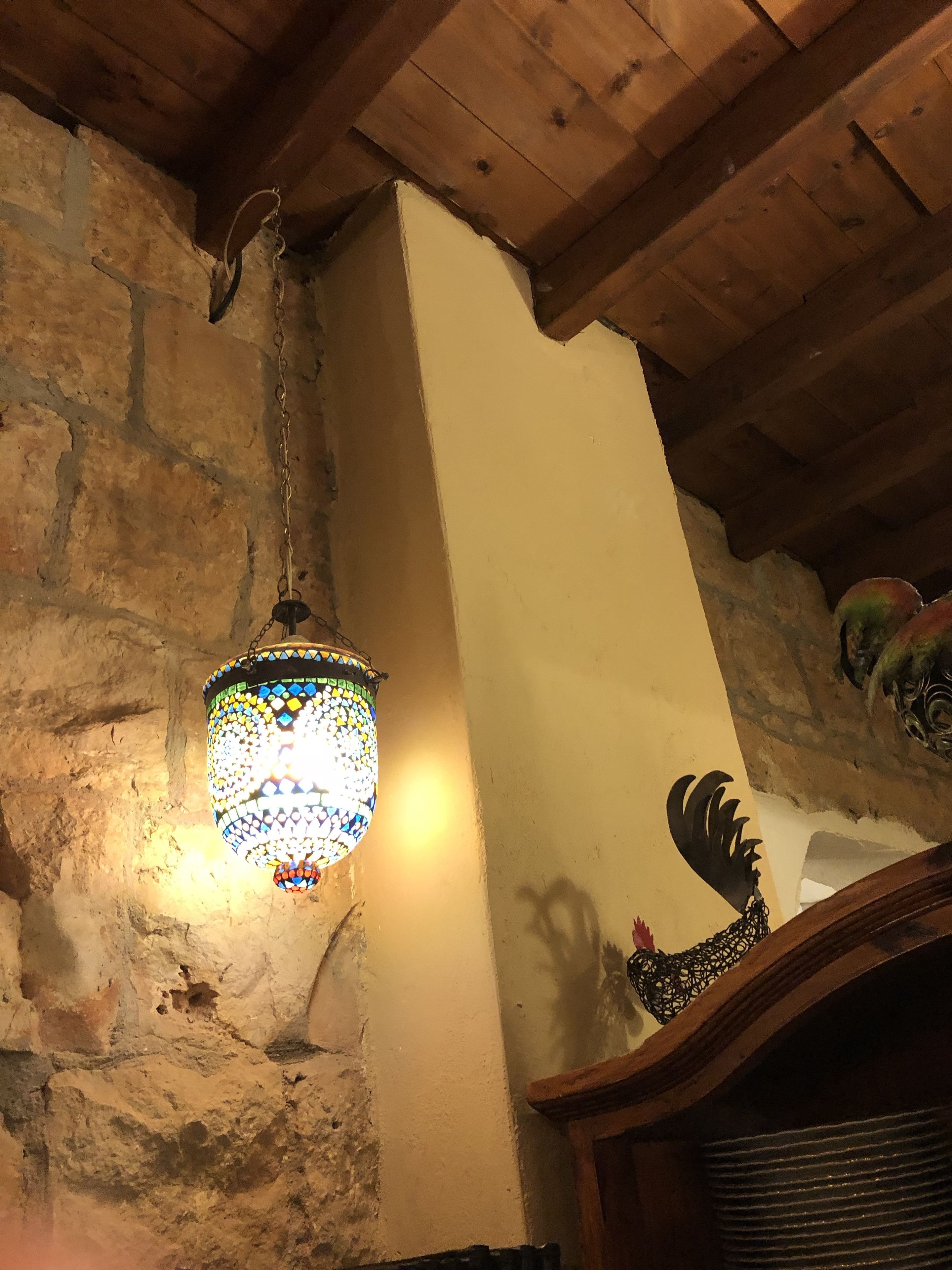 A rustic interior with a mosaic hanging light fixture, stone walls, and wooden beams.