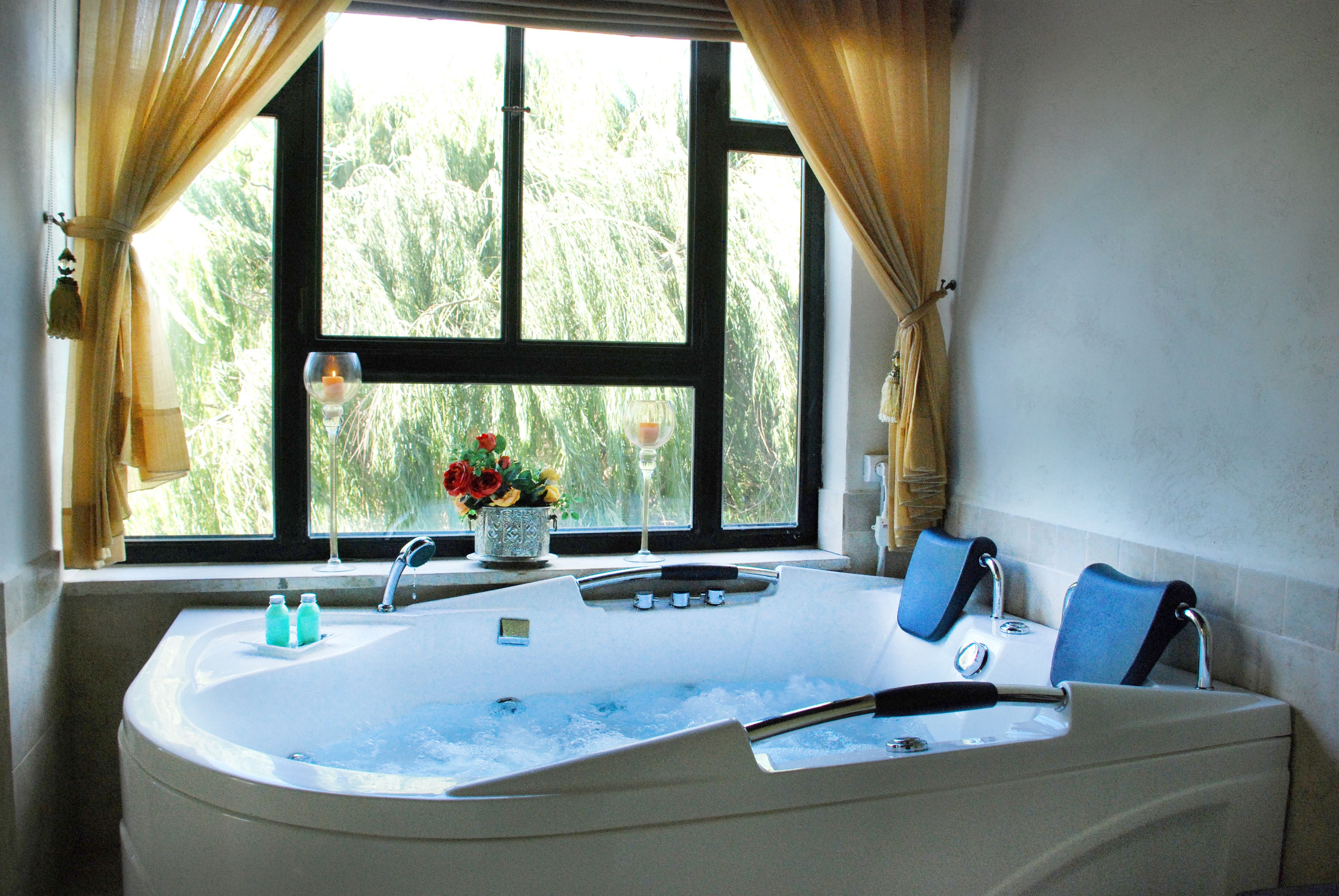 A bathroom with a large bathtub, a window with curtains, and a vase with flowers on the windowsill.