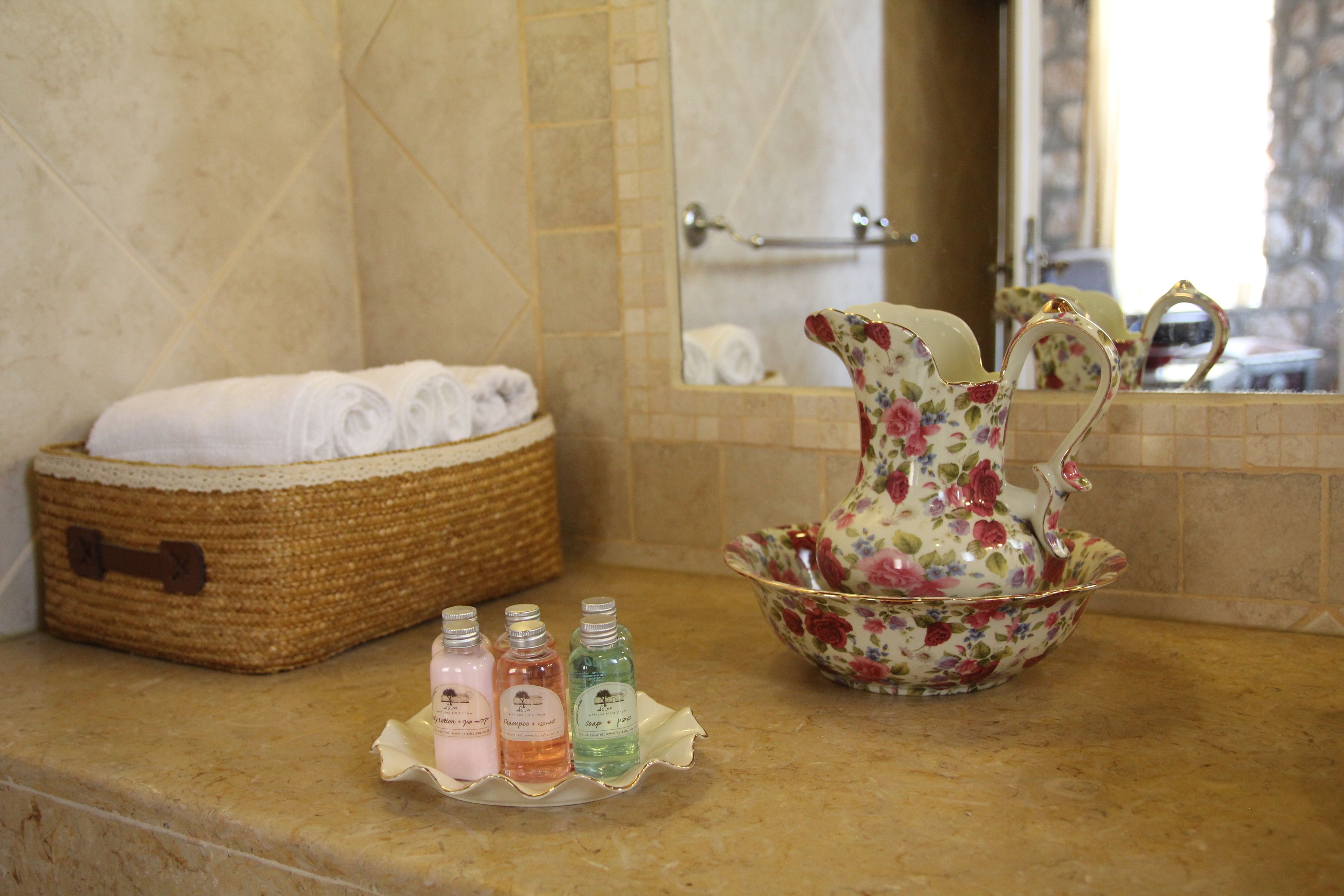 A bathroom with a woven basket of towels, a floral pitcher, and three bottles of soap on the counter.