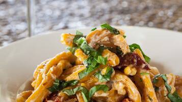 A plate of pasta with chicken and greens, a glass of white wine, and a textured table surface.