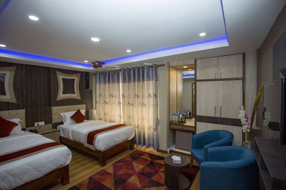 A hotel room with two beds, a desk, a chair, a TV, and a bathroom visible through an open door.