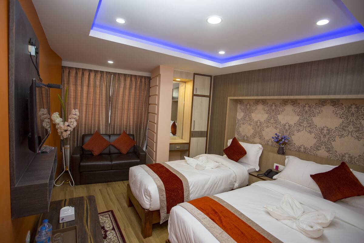 A hotel room with two beds, a sofa, a TV, and a mirror.