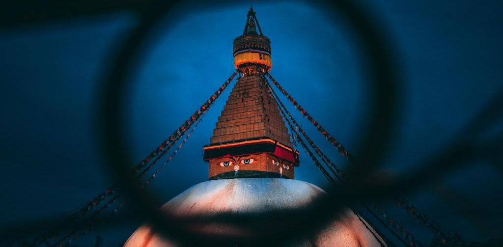 Ein Nachtblick auf das Boudhanath Stupa mit einem kreisförmigen Logo oben.