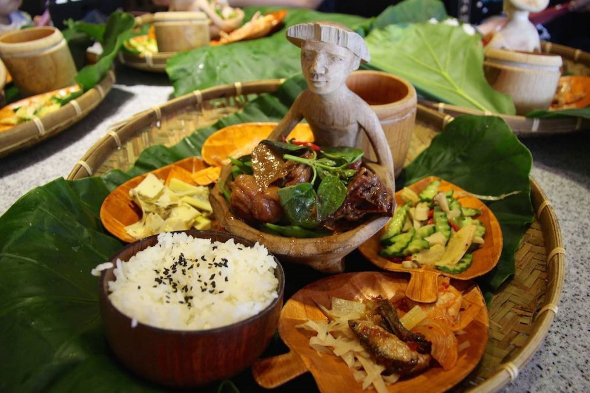 Ein traditionelles Essensarrangement mit verschiedenen Gerichten, darunter Reis, Gemüse und Fleisch, serviert auf einem gewebten Tablett.