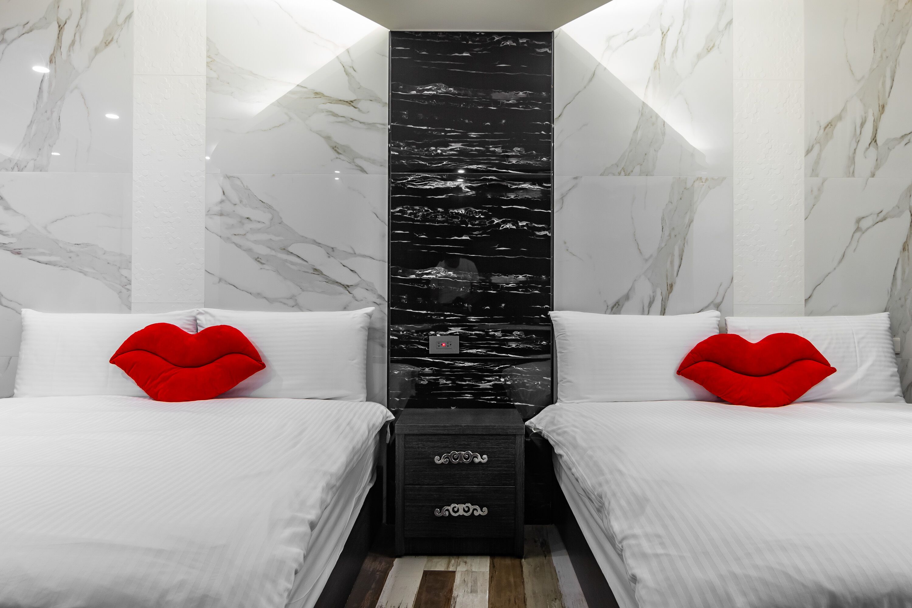 Una habitación de hotel moderna con dos camas, ropa de cama blanca y almohadas rojas en forma de corazón.