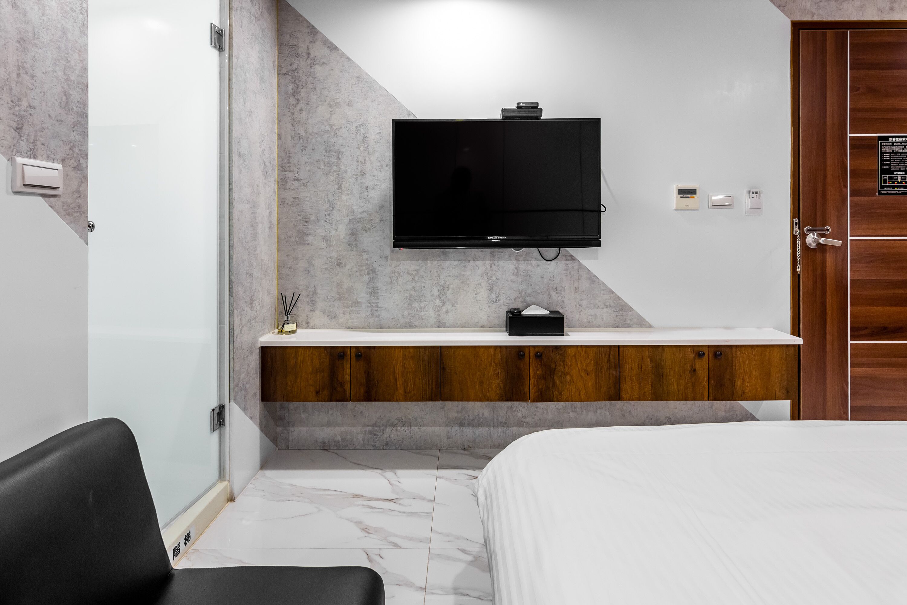 A modern hotel room with a large bed, a TV mounted on the wall, a wooden vanity, and a marble floor.