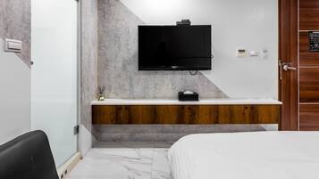 A modern hotel room with a large bed, a TV mounted on the wall, a wooden vanity, and a marble floor.