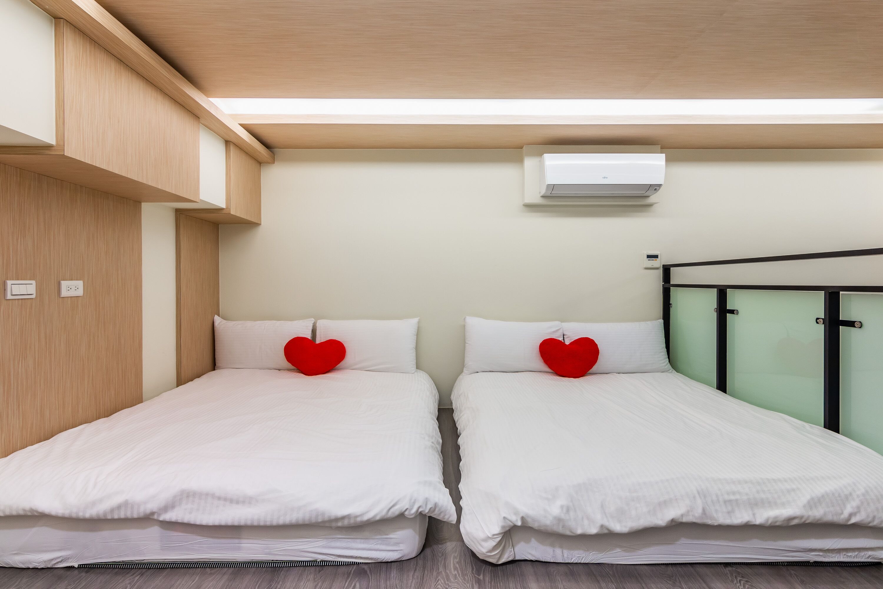 A twin room with two beds, a wooden wardrobe, an air conditioning unit, and a glass partition.