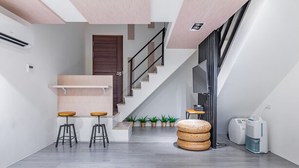 A modern interior with a staircase, a small seating area with stools, a round wicker ottoman, and a white air purifier. - Sun Moon Tea Hotel (Yuchi)