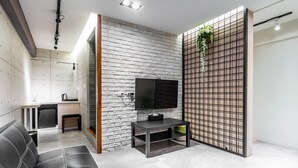 A modern living room with a black leather sofa, a TV on a stand, a kitchen area with a white brick wall, and a decorative plant. - Sun Moon Tea Hotel (Yuchi)