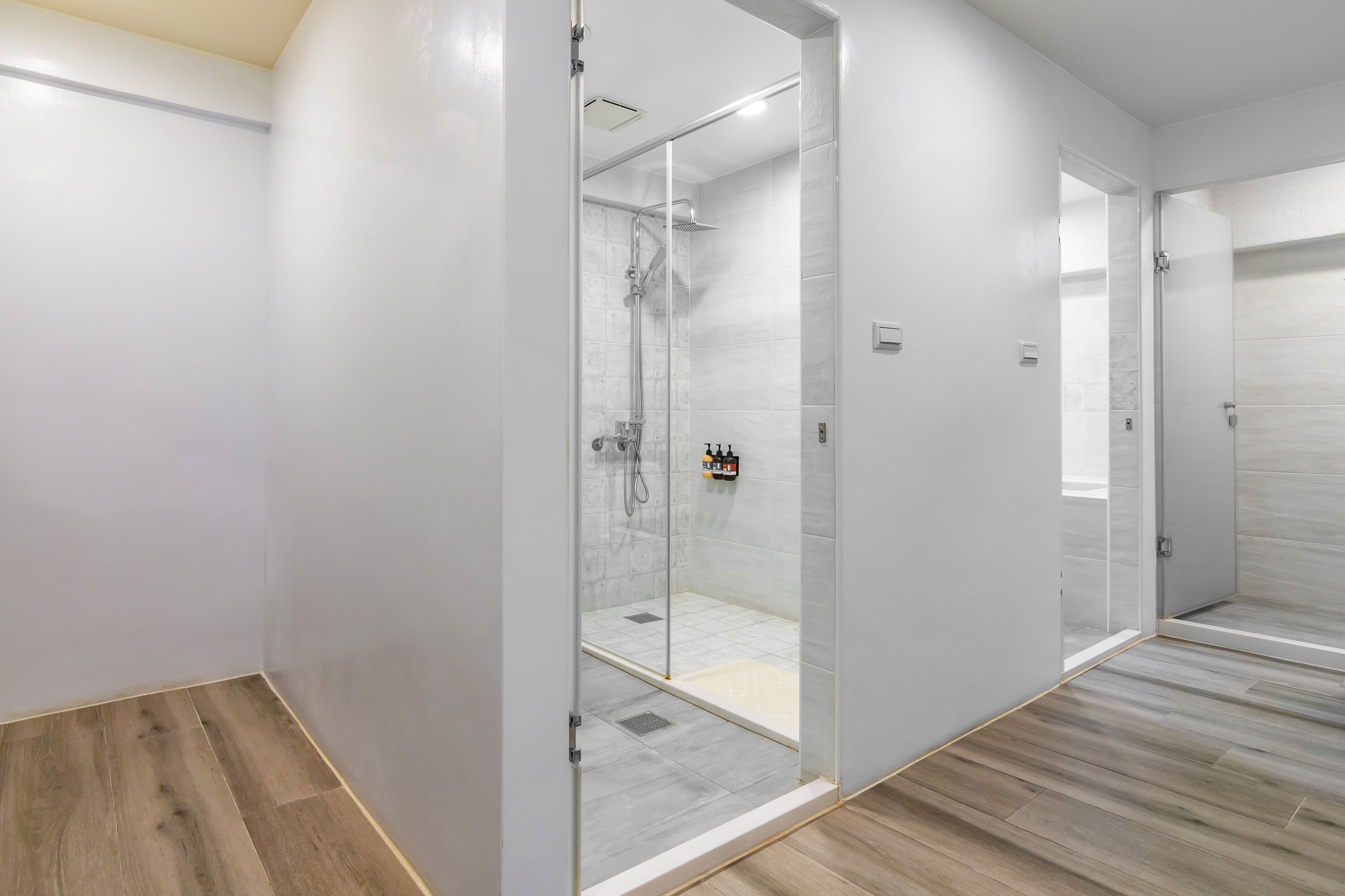 A modern bathroom with a glass-enclosed shower, a wooden floor, and white walls.