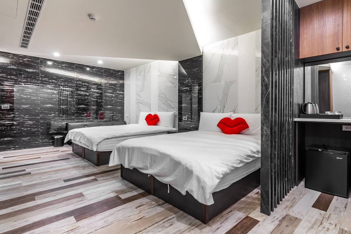 A modern bedroom with two beds, a small desk, and a mirror.