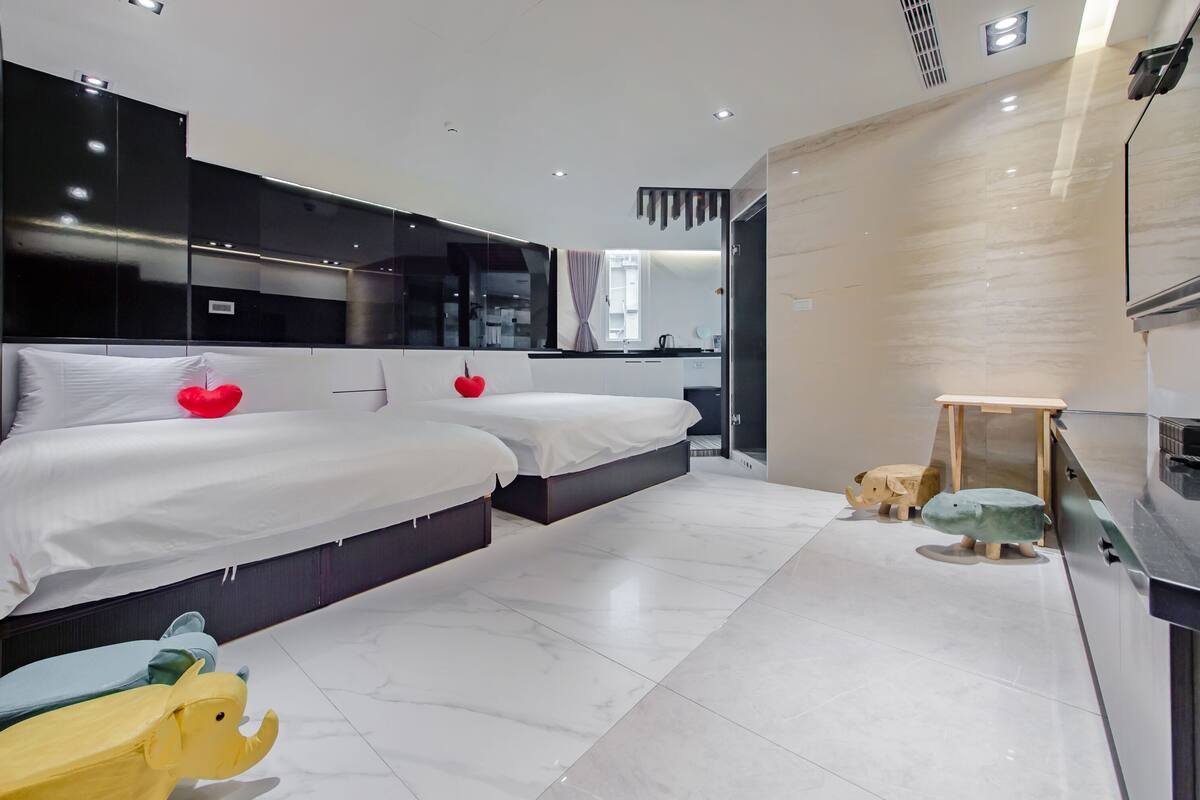 A modern bedroom with two beds, a small wooden table, and a refrigerator.