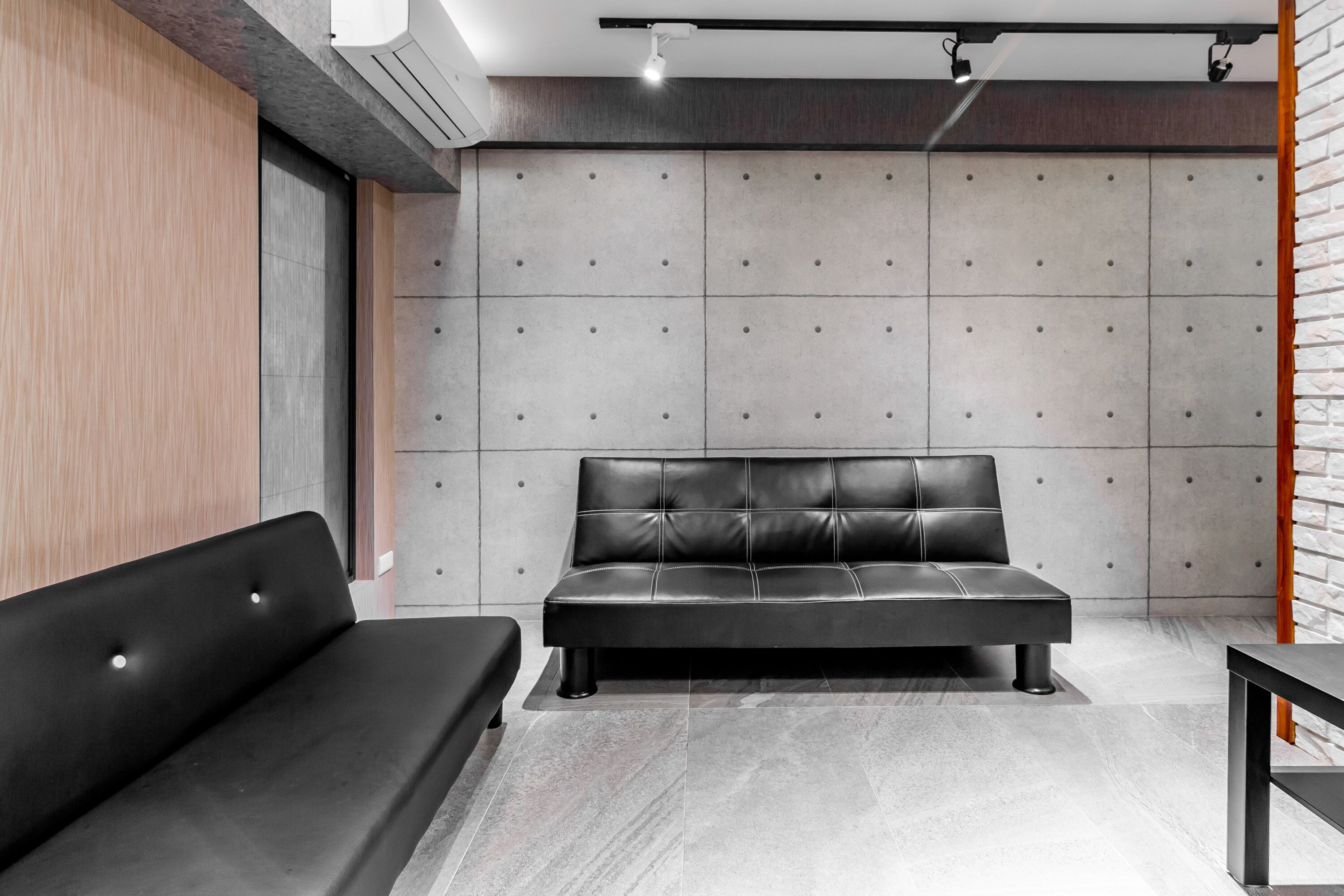 A modern room with a black leather sofa, a grey padded wall, and a wooden panel on the left.