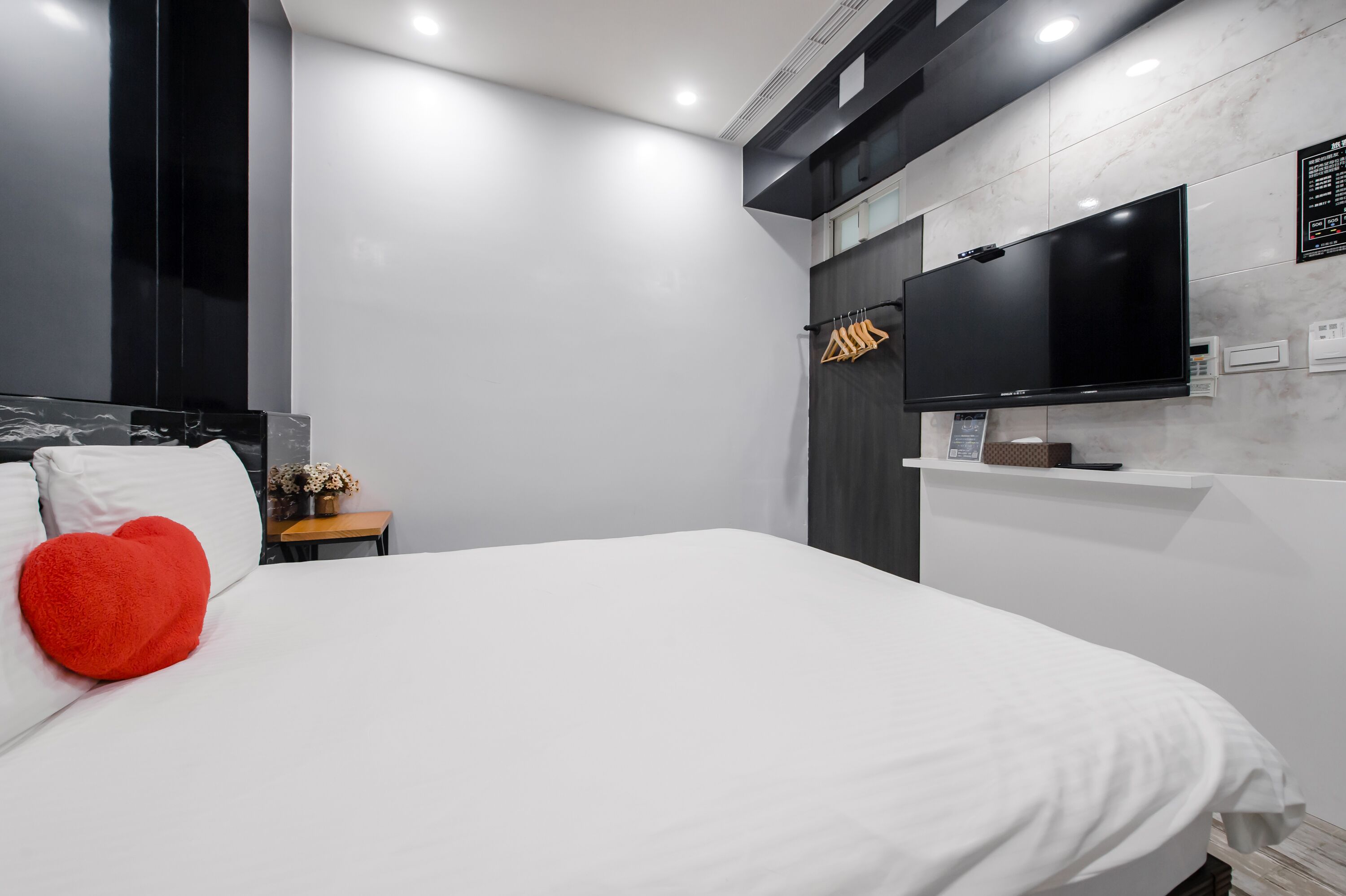 Una habitación de hotel moderna con una cama grande, un televisor de pantalla plana montado en la pared y una mesita de noche con un florero.