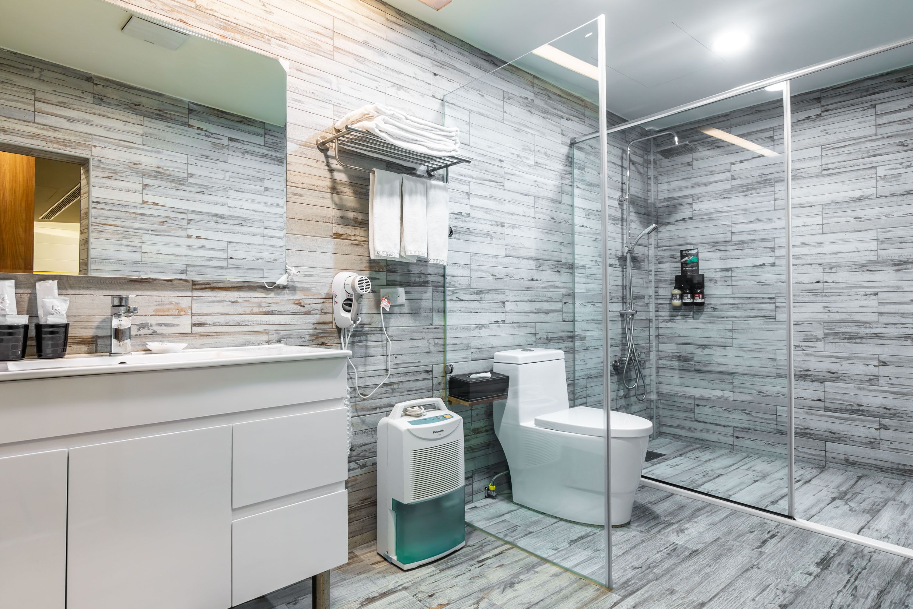 Een moderne badkamer met een marmeren wand, een douchecabine met glazen wanden, een witte wastafel en een toilet.