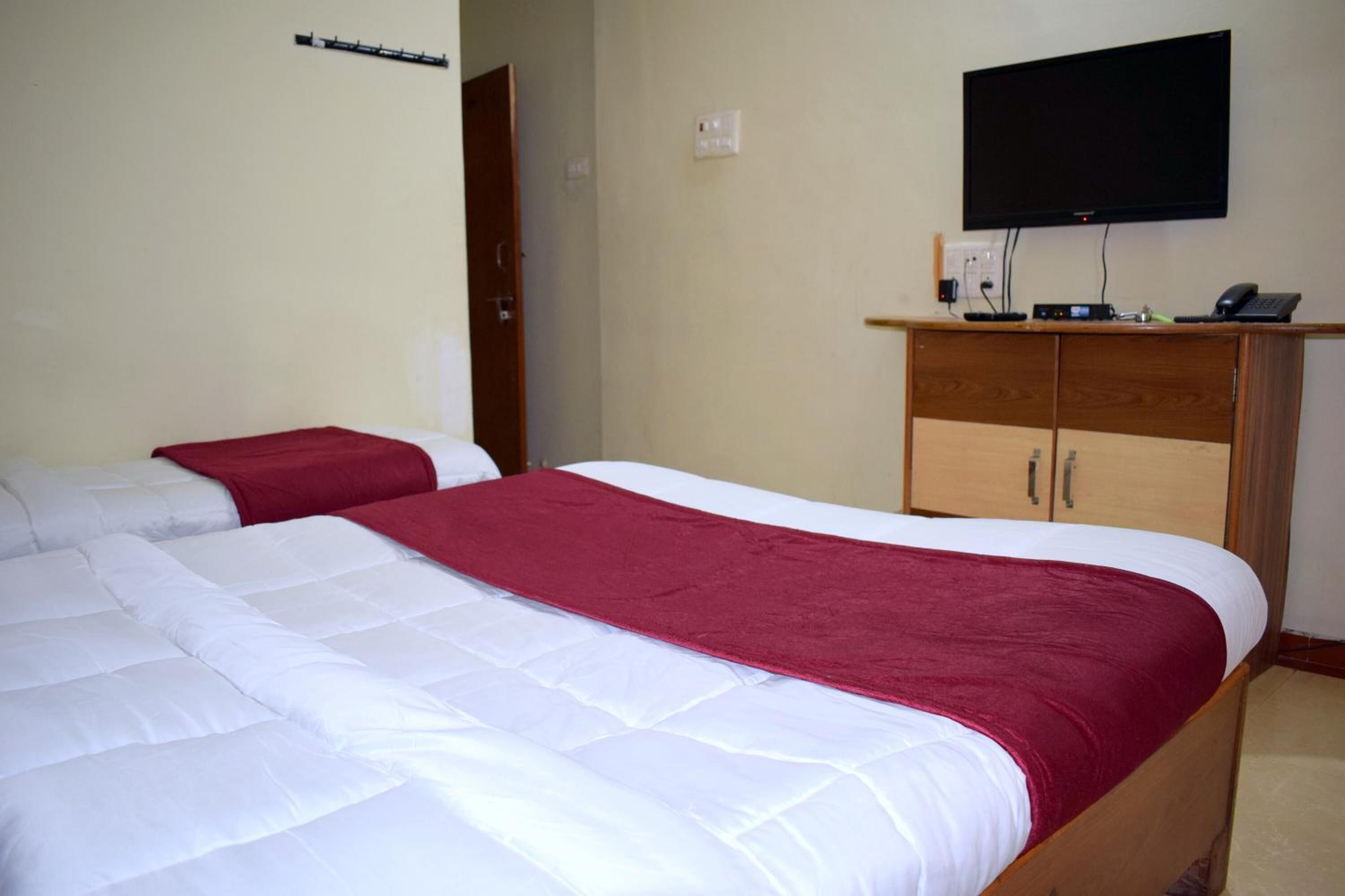 A hotel room with two beds, a television mounted on the wall, and a wooden cabinet with a flat-screen TV.