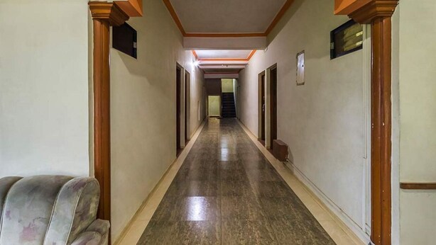 Um corredor comprido e estreito, com colunas de madeira e piso de mármore, que leva a uma escadaria.