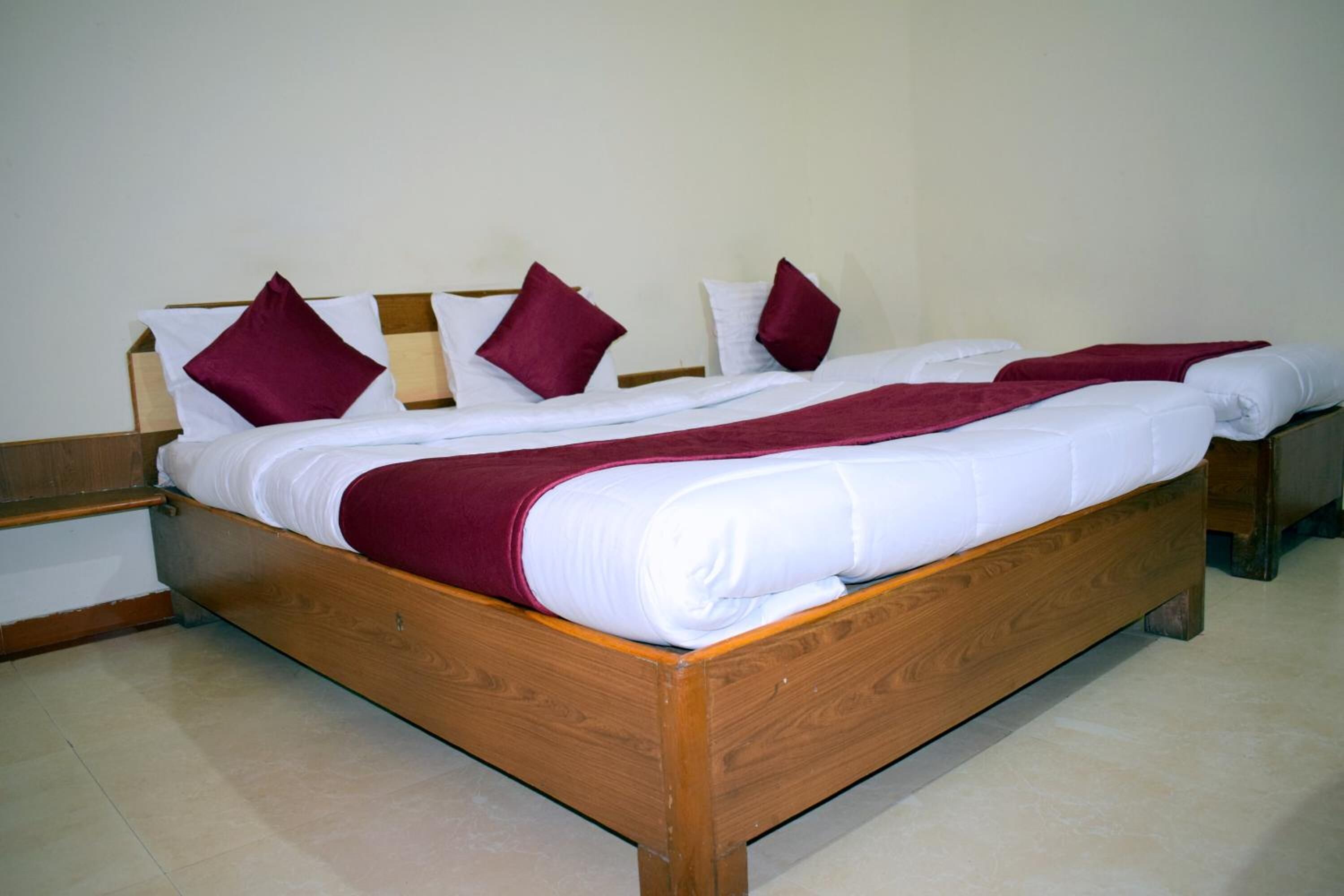 A wooden bed with white and maroon bedding, two nightstands, and a plain wall.
