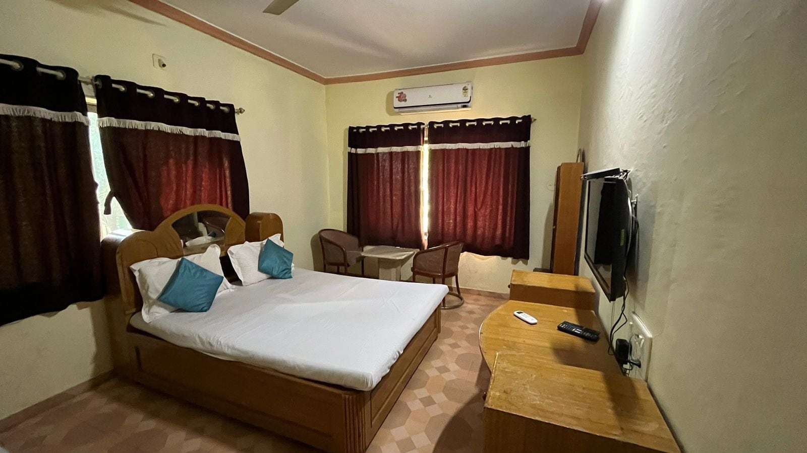 A hotel room with a bed, a desk, a chair, a television, and an air conditioning unit.