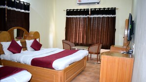 Quarto de hotel com cama de madeira, duas cadeiras, uma escrivaninha e uma televisão.