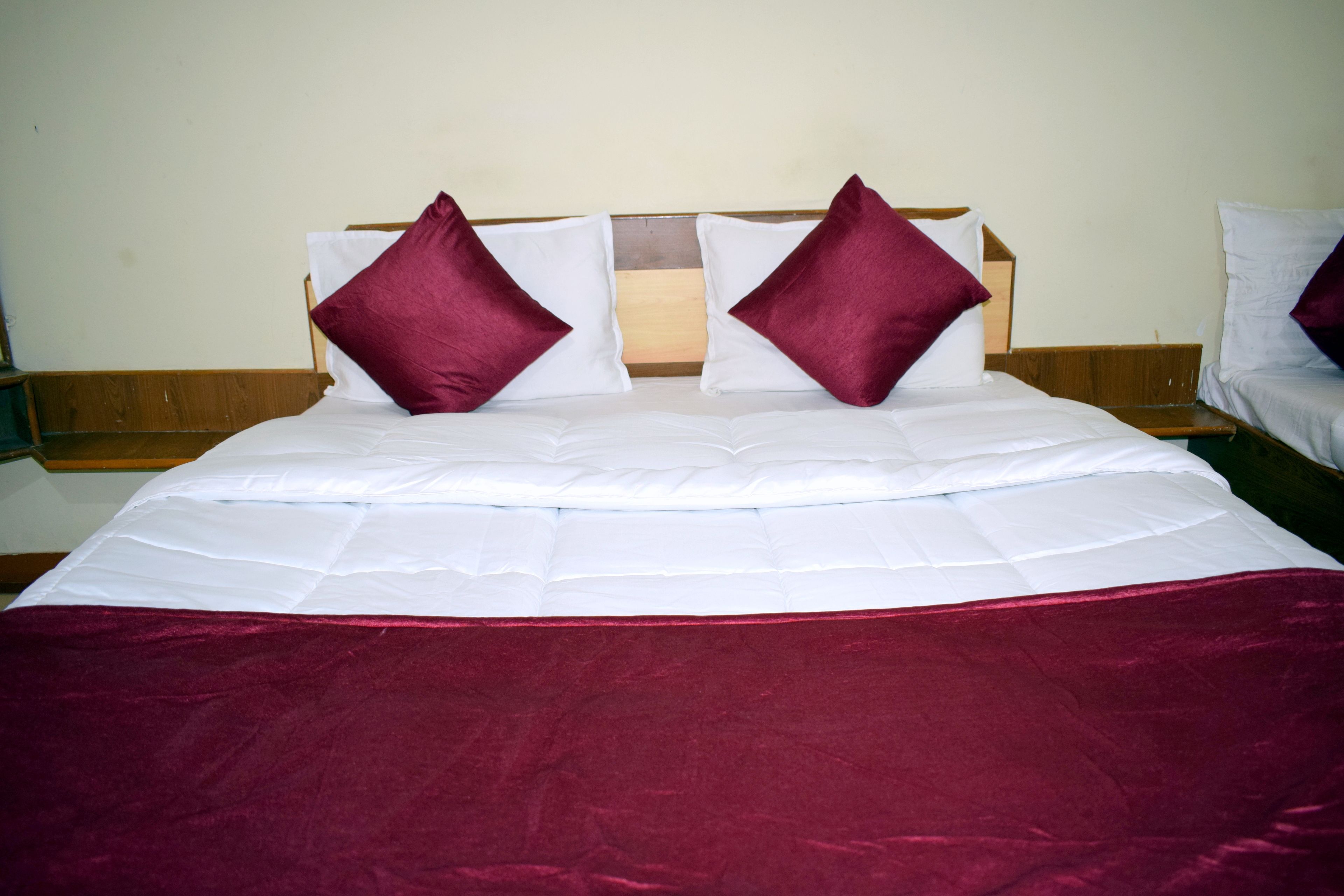 Una cama con cabecera de madera, dos almohadas y una colcha roja.