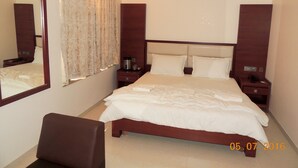Camera d'albergo con un letto grande, un comodino, una sedia e uno specchio.