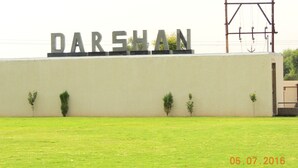 Un cartello con la scritta "DARSHAN" su un muro, circondato da piccole piante e una zona erbosa.