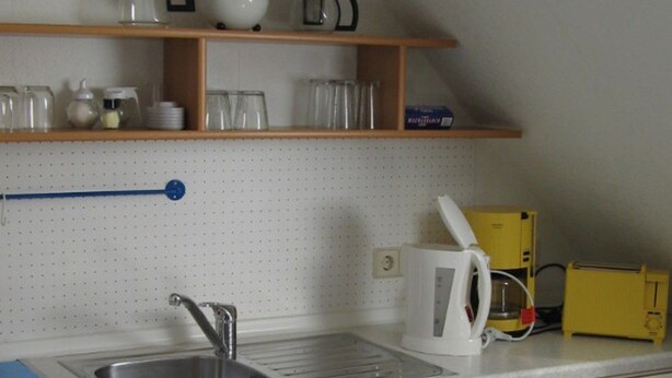 Uma cozinha com pia, armários, bancada e prateleira com utensílios.