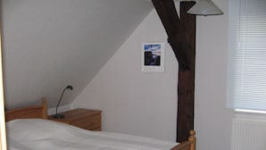 Quarto com cama de madeira, mesa de cabeceira, abajur e janela com persianas.
