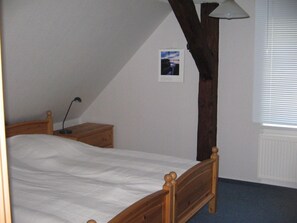 A bedroom with a wooden bed, a nightstand, a lamp, and a window with blinds.