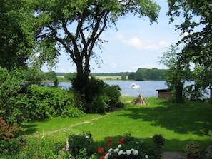 A garden with a large tree, a small shed, and a path leading to a lake with a boat.